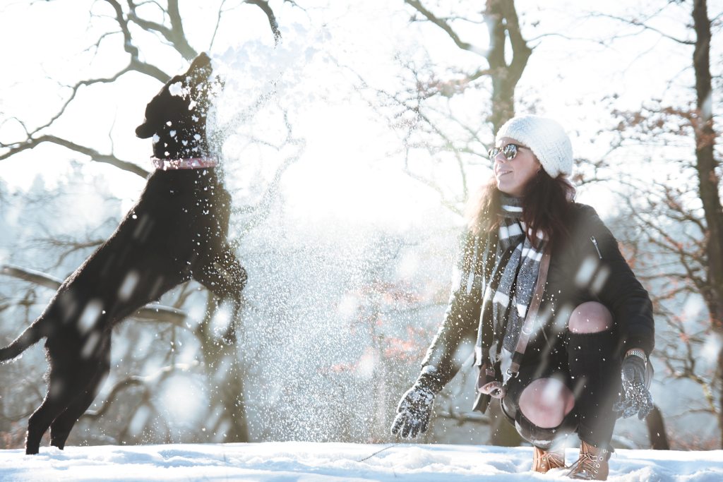 une jeune femme joue avec son chien dans la neige